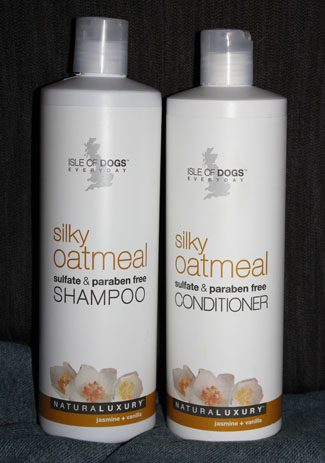 Two bottles of sleeky dogs shampoo and conditioner for dogs, labeled "silky oatmeal" and "sulfate & paraben free," placed against a textured gray background.