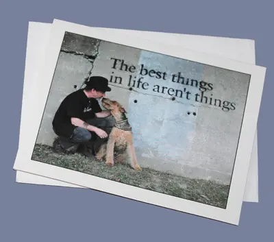 A photo of a man kneeling and affectionately touching foreheads with his dog beside a wall with the phrase, "the best things in life aren't things.