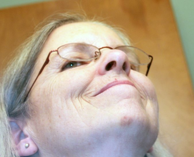 Close-up of an elderly woman with glasses looking upward, smiling slightly.